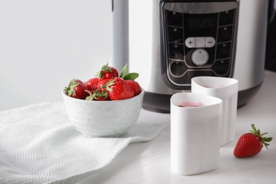 Cups of homemade yogurt, strawberries and multi cooker on table