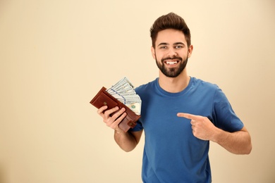 Photo of Happy young man with wallet full of money on color background. Space for text