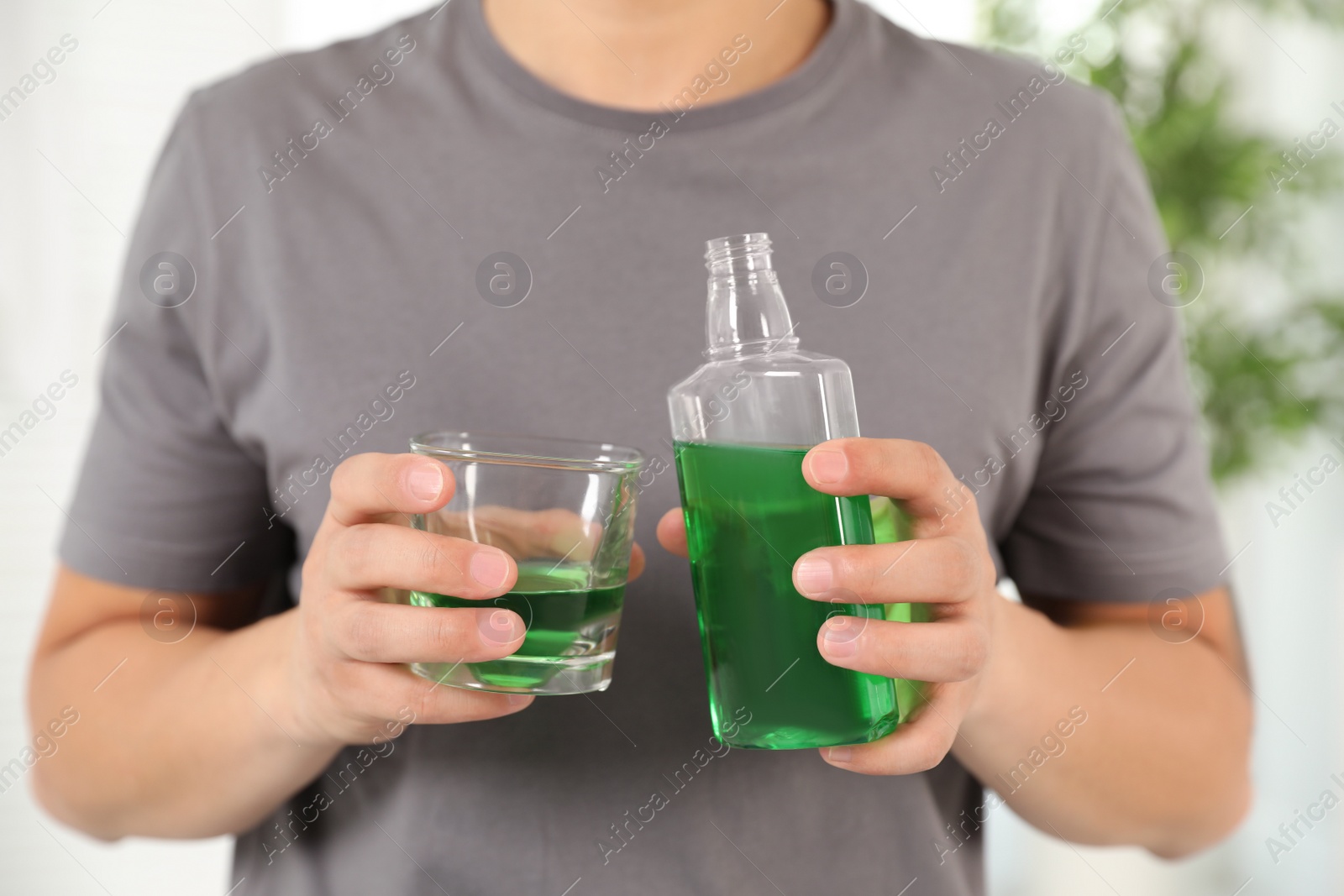 Photo of Man holding bottle and glass with mouthwash in bathroom, closeup. Teeth care