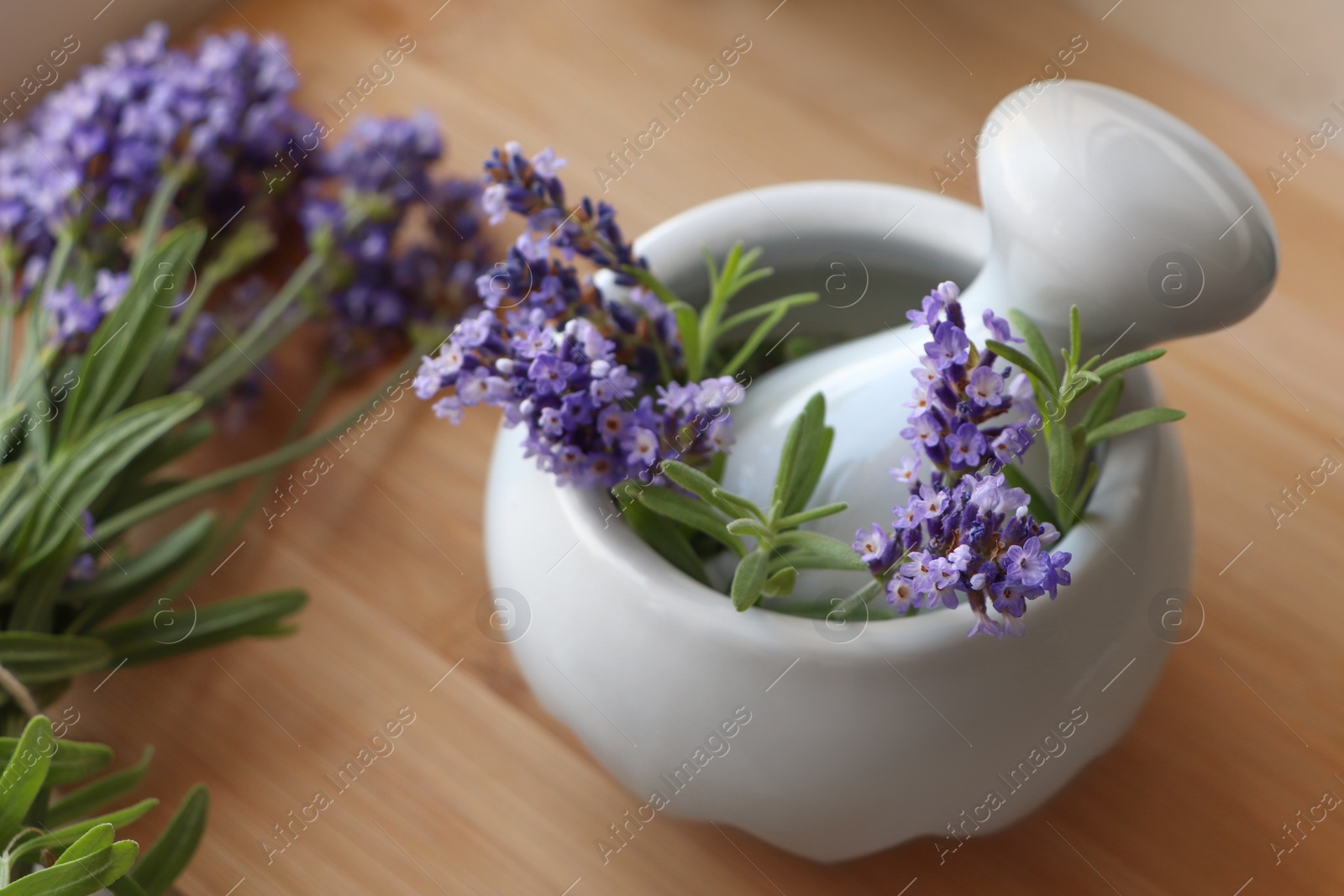 Photo of Mortar with fresh lavender flowers, rosemary and pestle on wooden table, closeup
