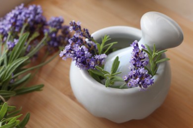 Photo of Mortar with fresh lavender flowers, rosemary and pestle on wooden table, closeup