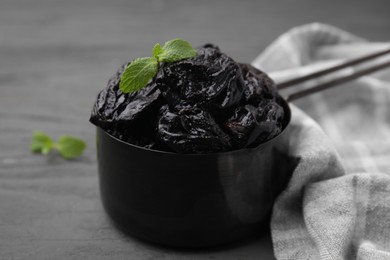 Photo of Sweet dried prunes and mint in scoop on grey wooden table, closeup