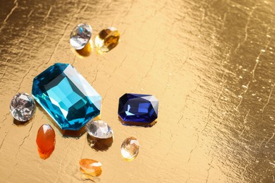 Photo of Different beautiful gemstones for jewelry on golden background, above view. Space for text