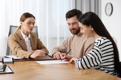 Couple signing document while having meeting with lawyer in office, selective focus