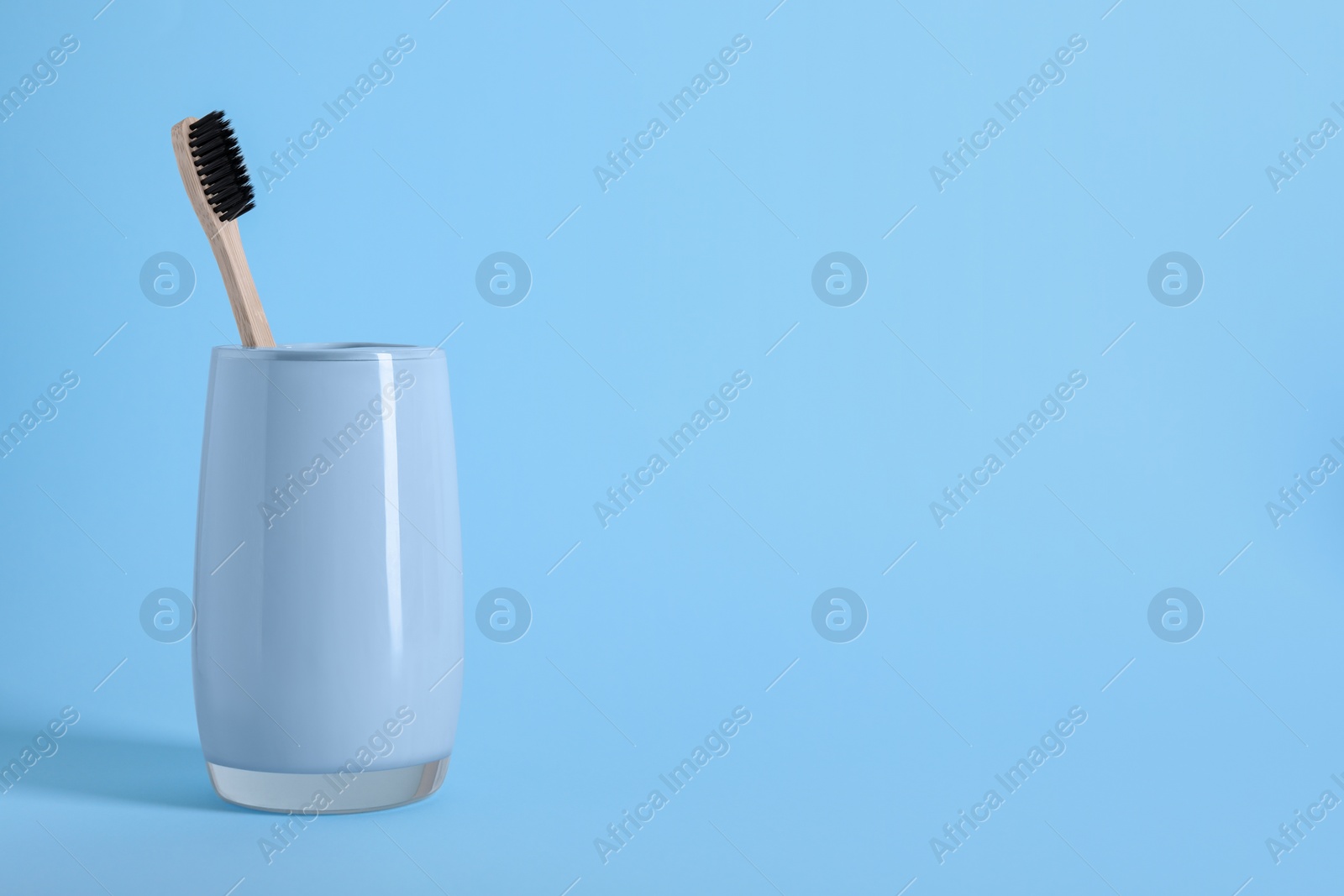 Photo of Bamboo toothbrush in holder on light blue background, space for text