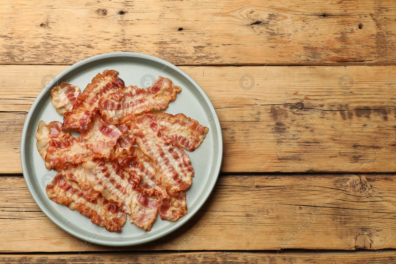 Photo of Delicious fried bacon slices on wooden table, top view. Space for text