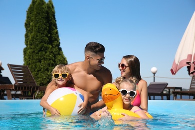 Photo of Happy family with inflatable ring and ball in outdoor swimming pool on sunny summer day