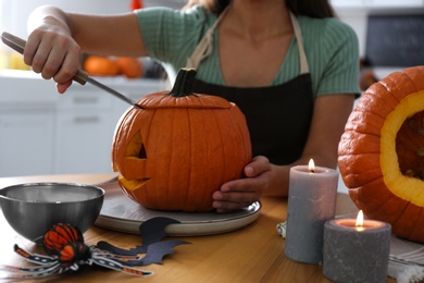 Photo of Woman making pumpkin jack o'lantern at table in kitchen, closeup. Halloween celebration