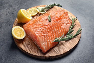Photo of Wooden board with raw salmon and ingredients for marinade on grey background