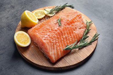 Wooden board with raw salmon and ingredients for marinade on grey background