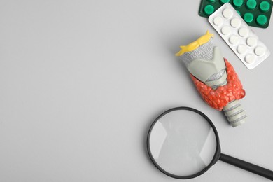 Photo of Plastic model of thyroid with tumor, pills and magnifying glass on grey background, flat lay. Space for text