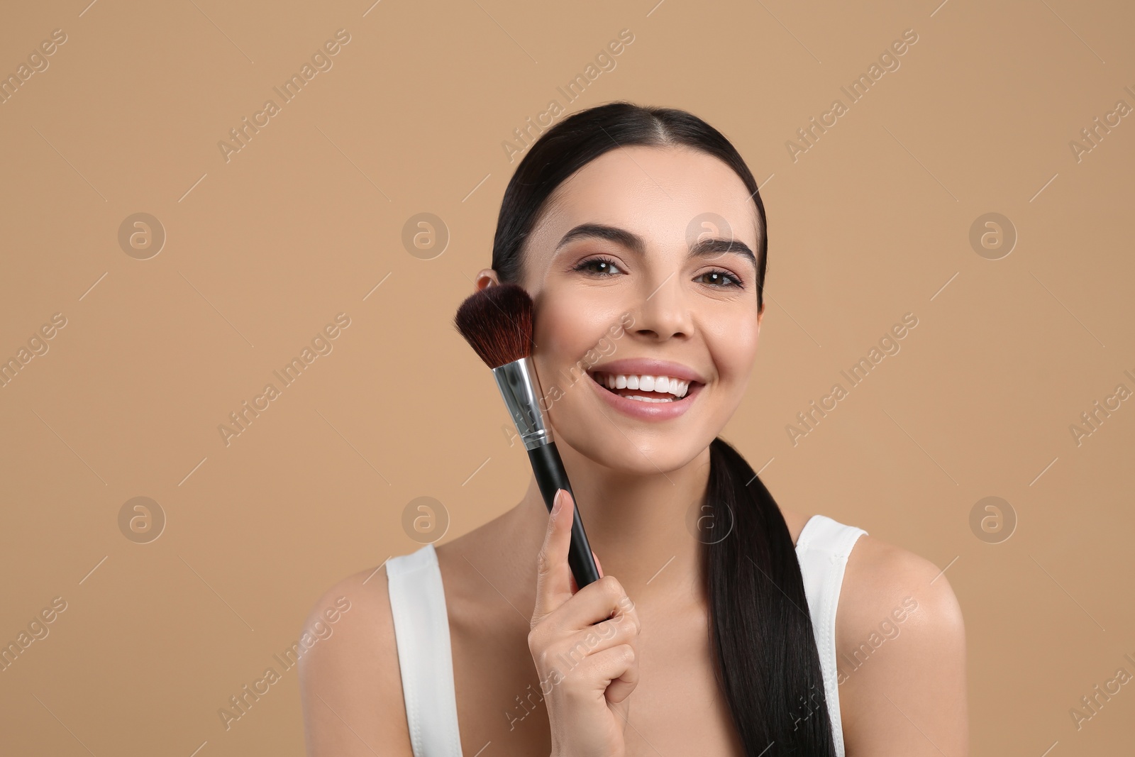 Photo of Beautiful woman with makeup brush on light brown background. Space for text