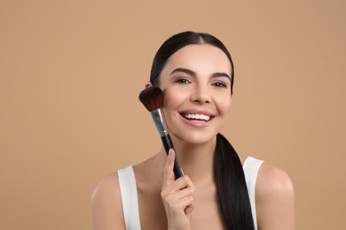Photo of Beautiful woman with makeup brush on light brown background. Space for text