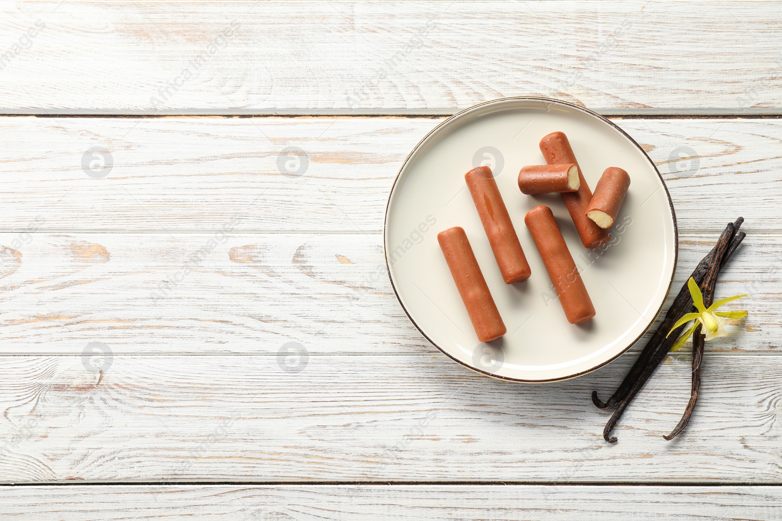 Photo of Glazed curd cheese bars, vanilla pods and flower on white wooden table, top view. Space for text