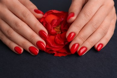Woman with red polish on nails touching flower on black background, closeup