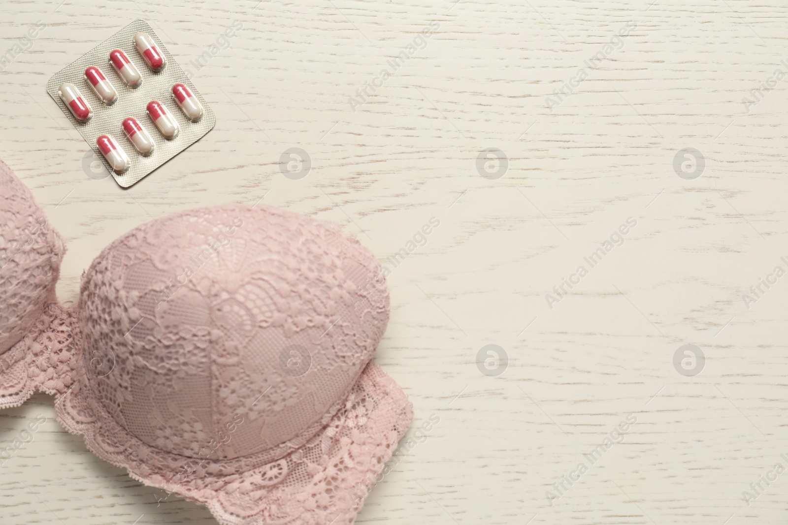 Photo of Breast cancer awareness. Bra and pills on white wooden table, flat lay. Space for text