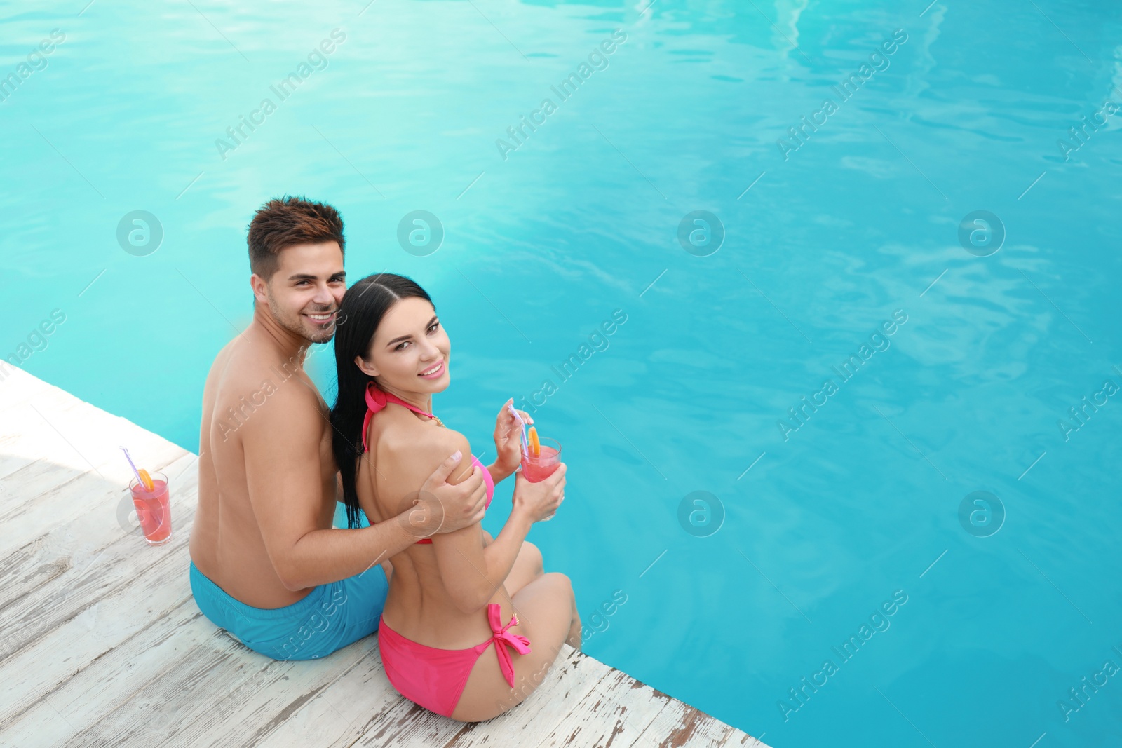 Photo of Woman in bikini with boyfriend near outdoor pool. Happy young couple