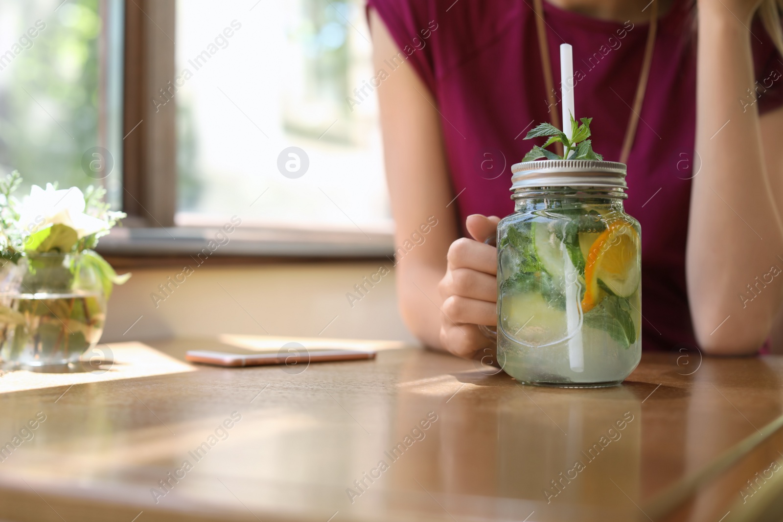 Photo of Young woman with mason jar of tasty natural lemonade in cafe, closeup. Detox drink