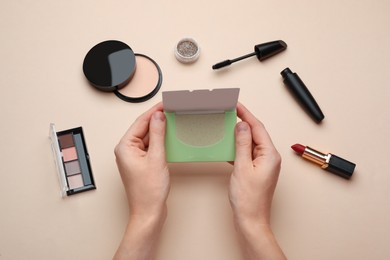 Woman with package of oil blotting tissues and decorative cosmetics on beige background, top view. Mattifying wipes