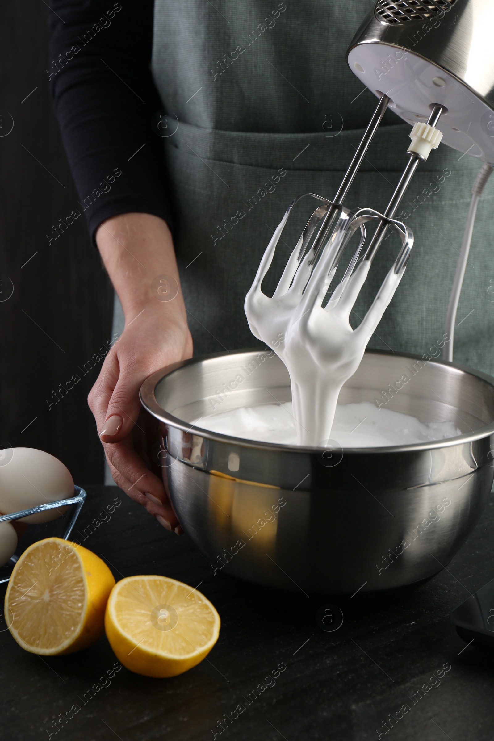 Photo of Woman making whipped cream with hand mixer at black table, closeup