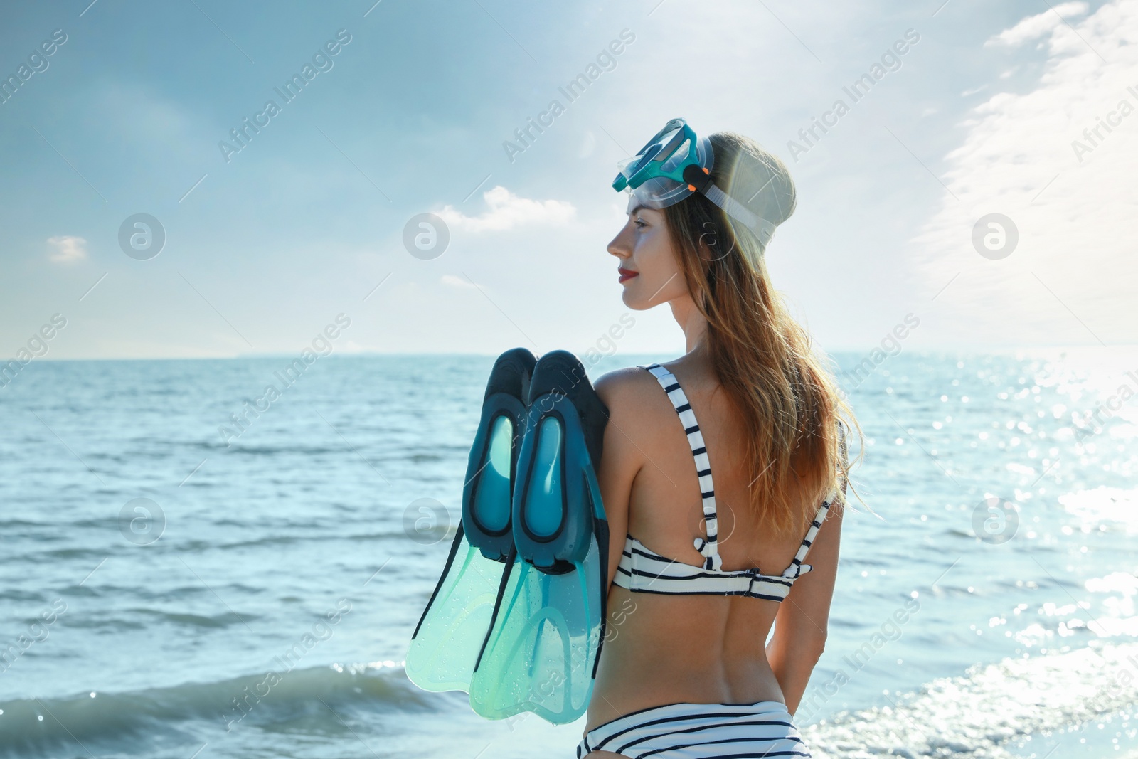 Photo of Woman with flippers and diving mask near sea on beach, back view
