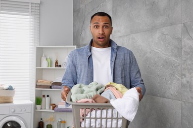 Photo of Emotional man with basket full of laundry in bathroom