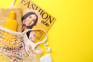 String bag with fashion magazine and beach accessories on yellow background, flat lay. Space for text