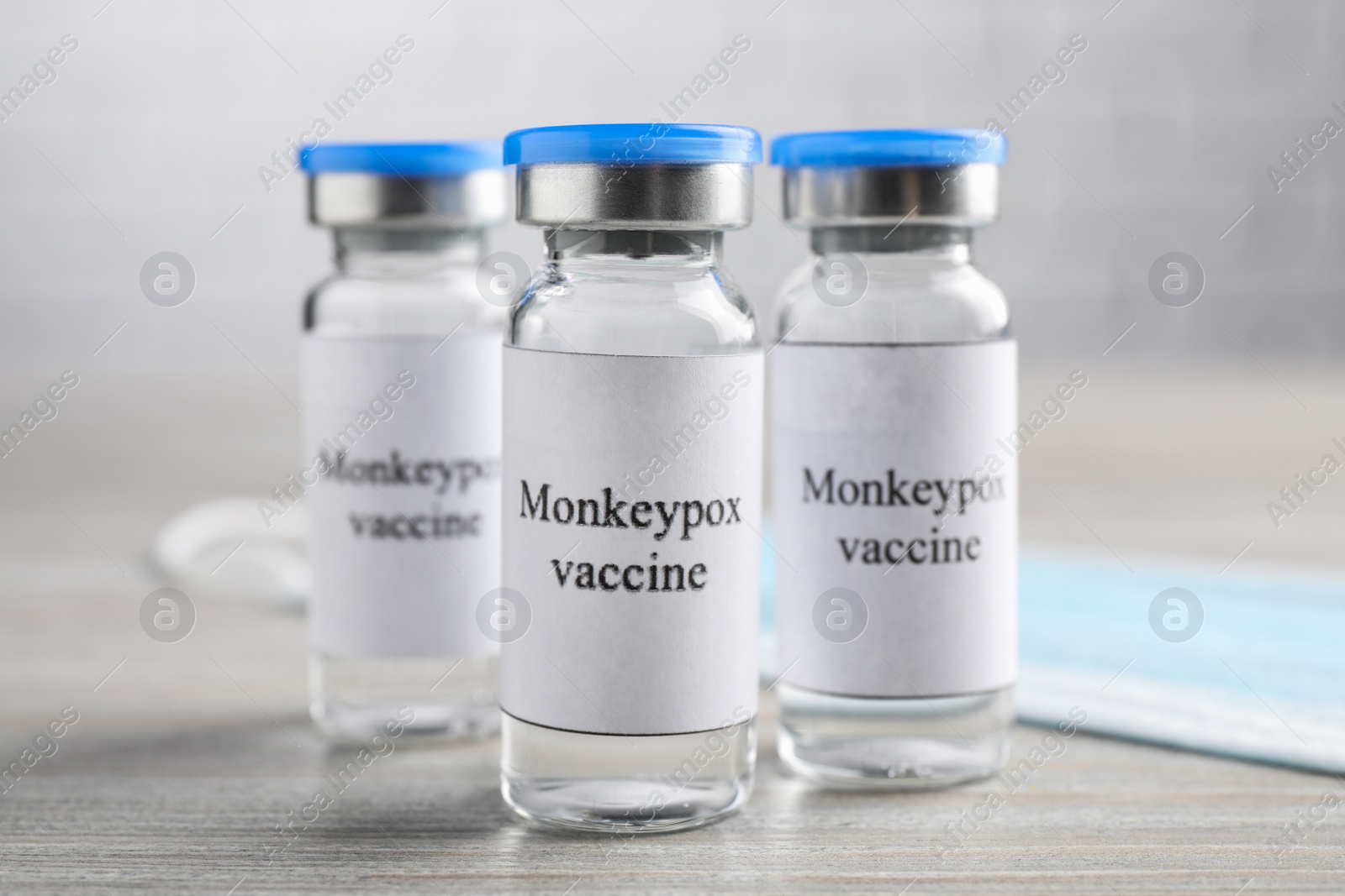 Photo of Monkeypox vaccine in glass vials and medical mask on wooden table