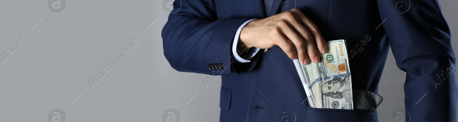 Image of Man putting bribe into pocket on grey background, closeup with space for text. Banner design