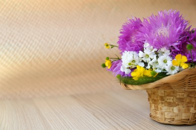 Photo of Bouquet of beautiful wildflowers in wicker basket on wooden table. Space for text