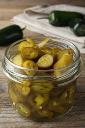 Glass jar with slices of pickled green jalapeno peppers on wooden table
