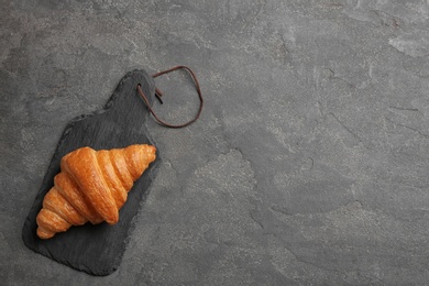 Photo of Slate board with tasty croissant and space for text on grey background, top view. French pastry