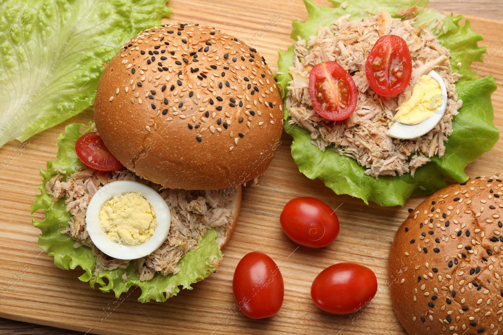 Photo of Delicious sandwiches with tuna, boiled egg and vegetables on wooden board, above view