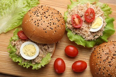 Photo of Delicious sandwiches with tuna, boiled egg and vegetables on wooden board, above view