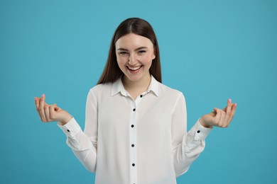 Happy woman showing money gesture on light blue background