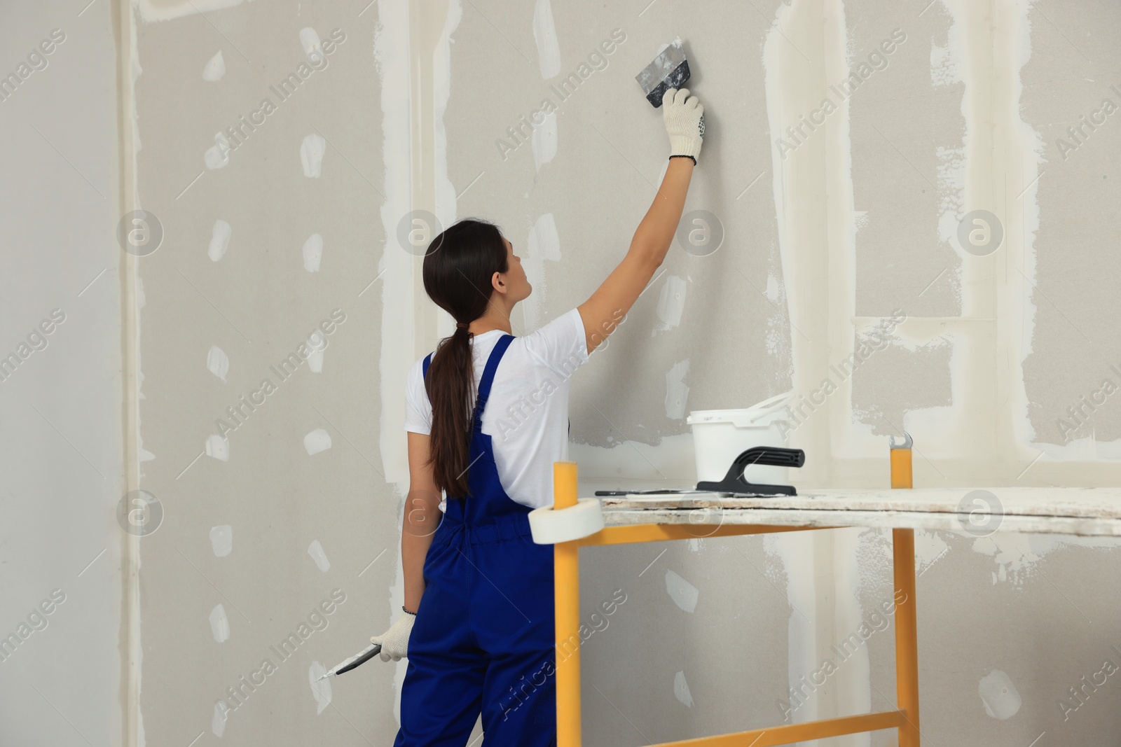 Photo of Worker plastering wall with putty knife indoors