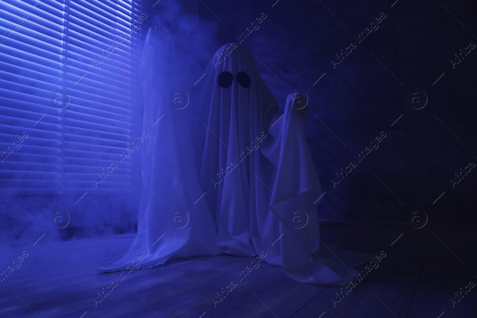 Photo of Creepy ghost. Woman covered with sheet near window in blue light