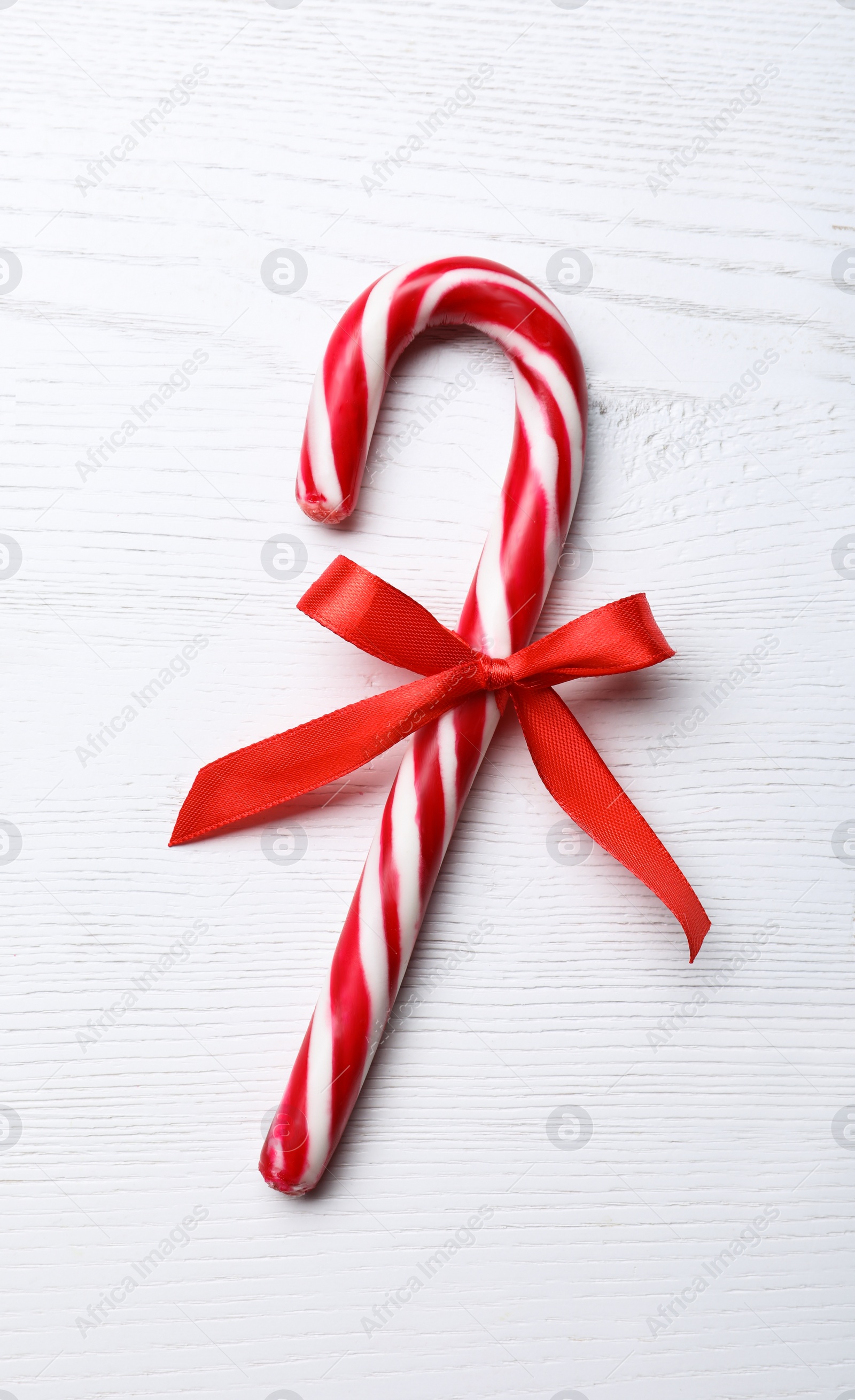 Photo of Sweet Christmas candy cane with bow on white wooden table, top view