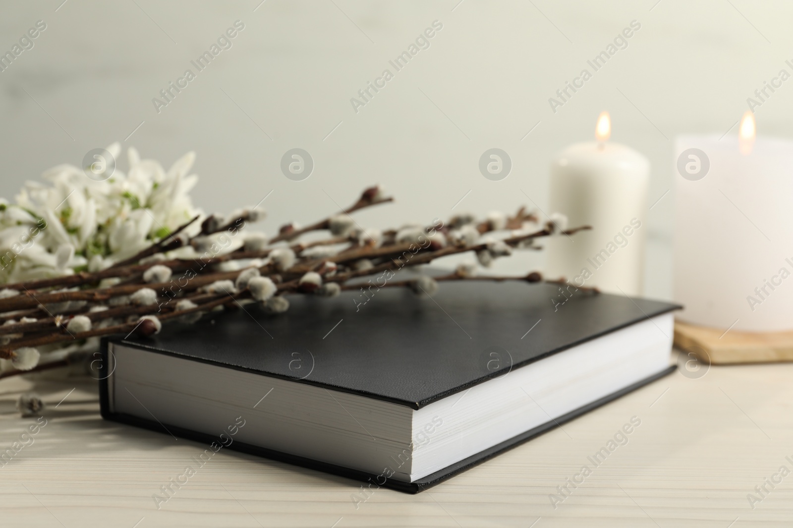 Photo of Bible, snowdrops, church candles and willow branches on white wooden table, closeup