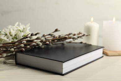 Photo of Bible, snowdrops, church candles and willow branches on white wooden table, closeup
