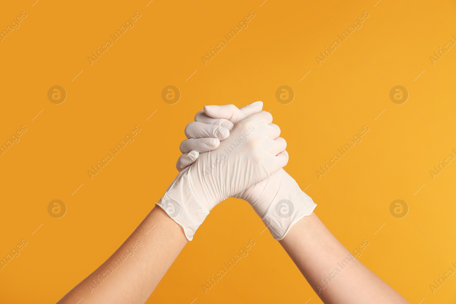 Photo of Doctors in medical gloves shaking hands on yellow background, closeup