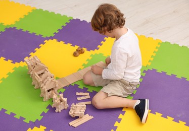 Photo of Little boy playing with wooden construction set on puzzle mat indoors. Child's toy