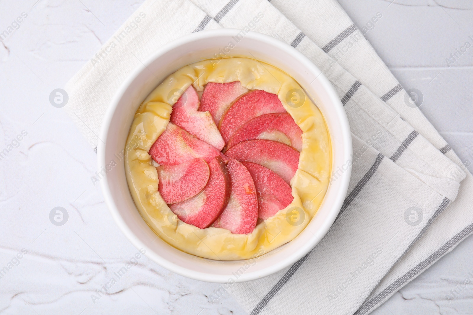 Photo of Baking dish with fresh dough and apples on white textured table, top view. Making galette