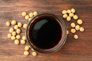 Photo of Soy sauce in bowl and soybeans on wooden table, flat lay