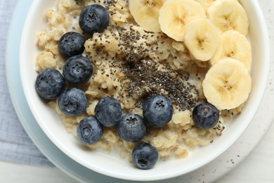 Tasty oatmeal with banana, blueberries and chia seeds served in bowl on white wooden table, top view