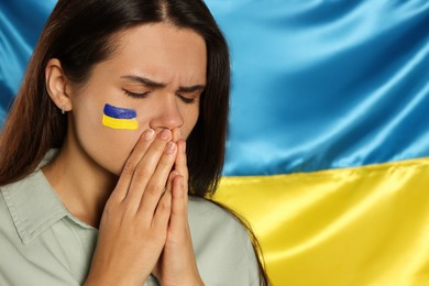 Sad young woman with clasped hands near Ukrainian flag, closeup. Space for text