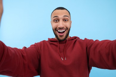 Photo of Smiling young man taking selfie on light blue background