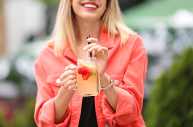 Young woman with mason jar of tasty lemonade outdoors