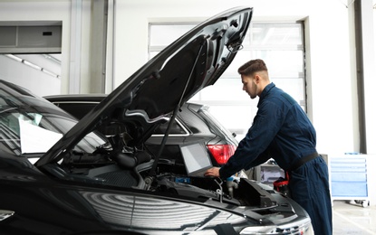 Technician checking car with laptop at automobile repair shop