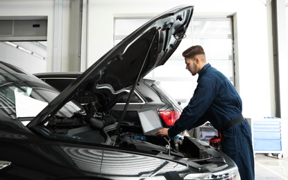 Photo of Technician checking car with laptop at automobile repair shop